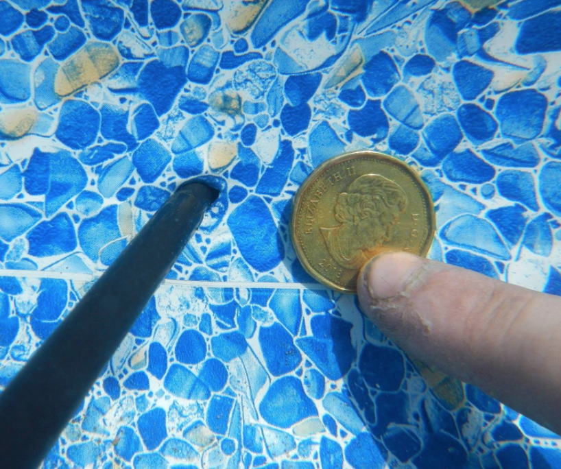 inside a pool with a skinny black tool and loonie beside to show leak