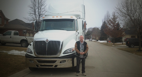 Man standing in front of a large truck parked on the road with snow on the ground