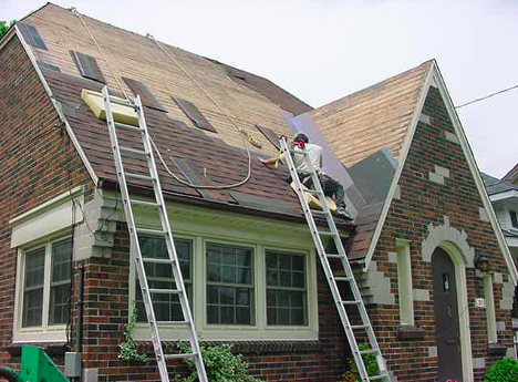 man on a roof with two ladders surrounding him putting up shingles