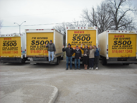 group of people standing in front of four yellow trucks with hands waving at camera