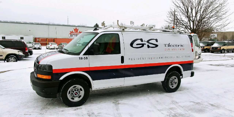 a trades van with company name, roof rack and a black and red stripe parked in the snow outside of a building