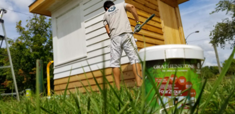 man painting a shed white with a large rolling paint brush