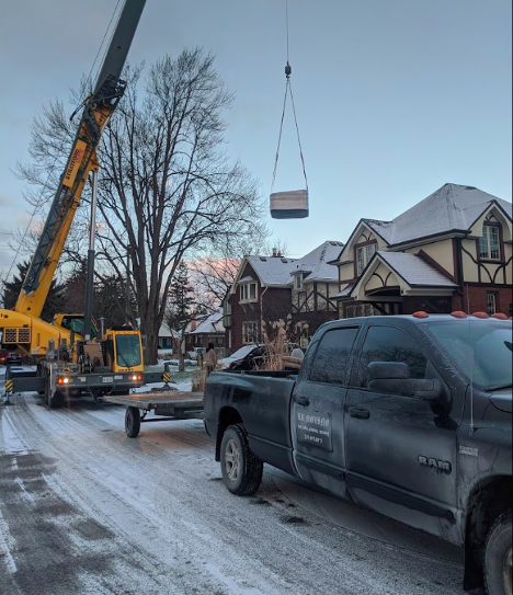 large crane lifting a square object onto a truck trailer with snow on the ground