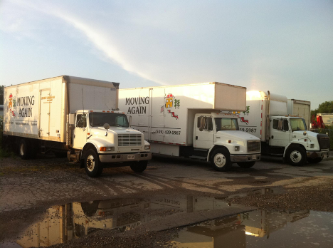 three large white trucks parked in a parking lot with large puddle in front on a sunny day