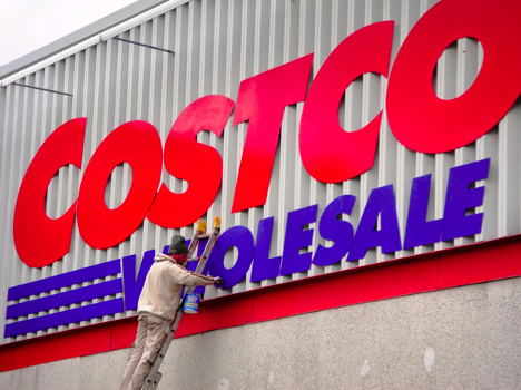 man painting a costco sign standing on a ladder