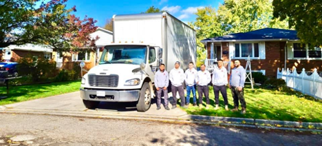six people standing on a driveway and front lawn beside a large white truck parked in the driveway of a house