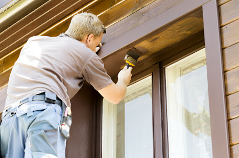 man painting the under trim of an outer door brown with a large paint brush