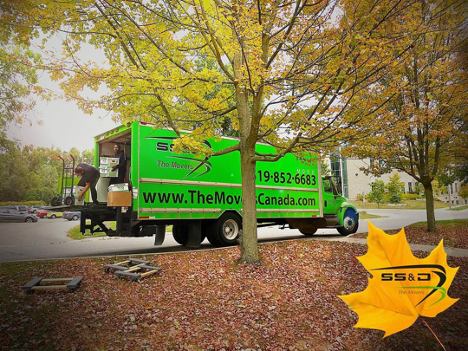 large green truck parked on the road with a man getting a dolly with many leaves on the ground in front