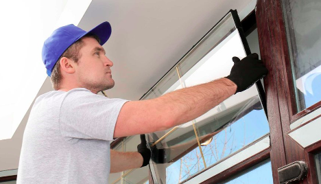 man placing a piece of glass into a window frame with black gloves on
