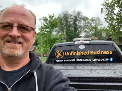 man smiling at the camera standing in front his branded work truck on an overcast day
