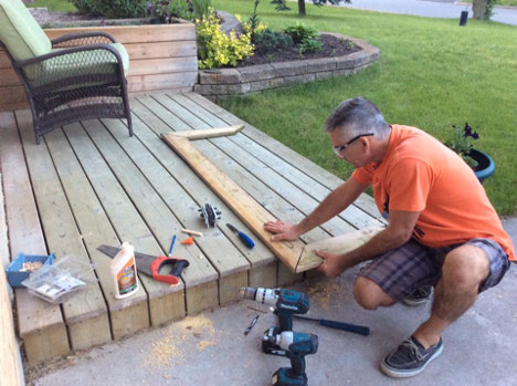 man putting two pieces of wood together on a deck in the shape of a frame with various tools around him