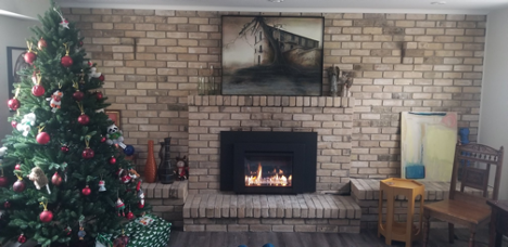 a living room with a Christmas tree on the left with a lit fireplace