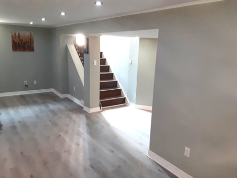 light grey vinyl flooring in a basement with view of stairs going up to bright door
