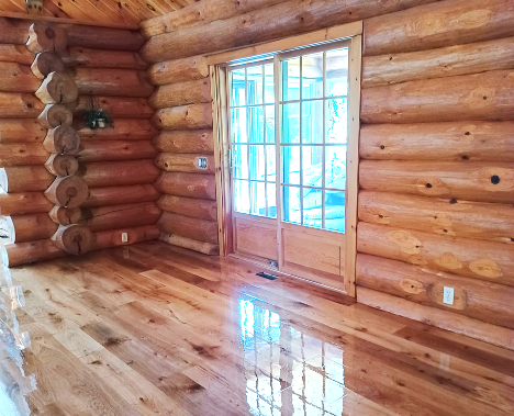 very shiny light hardwood floor panels in a log cabin with view of large window letting light in