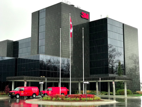 exterior of a large dark building with company logo on the top and two red trucks parked near front entrance