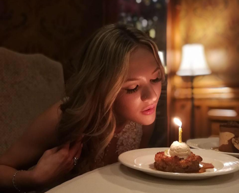 woman blowing out a candle on a piece of dessert