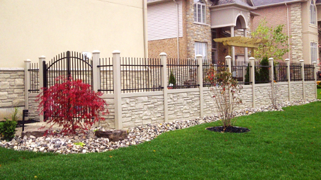 Large stone fence with iron bar feature along the top along the side of a house