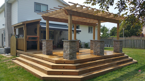 backyard deck feature with pergola feature set by stone pillars and four steps down to backyard