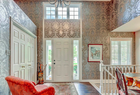 olden style entryway of a home with patterned wallpaper and red chair facing the door