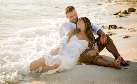 Young couple sitting on the sand just touching the water with woman leaning on man