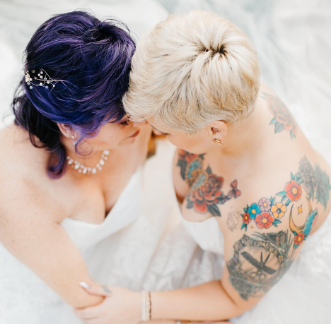 Two women in bridal gowns touching foreheads embracing