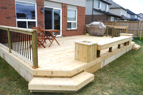 backyard deck with iron rod railing, seating area, and two garden beds on either side with three step walk down to lawn