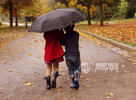 two young children walking away from camera holding an umbrella on a rainy day