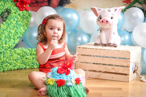 young girl sitting on the ground surrounded by balloons and other pieces of decor eating a cake in front of her