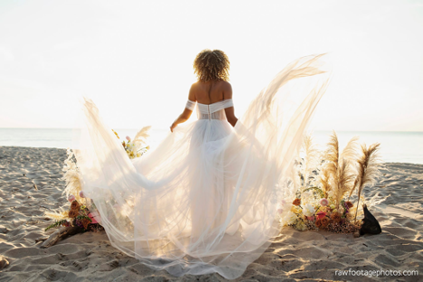 woman walking towards water at a beach with wedding dress flailing behind her at sunset