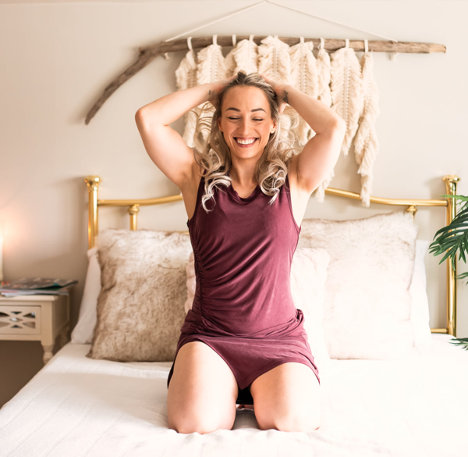 woman sitting on bed with hands in hair smiling