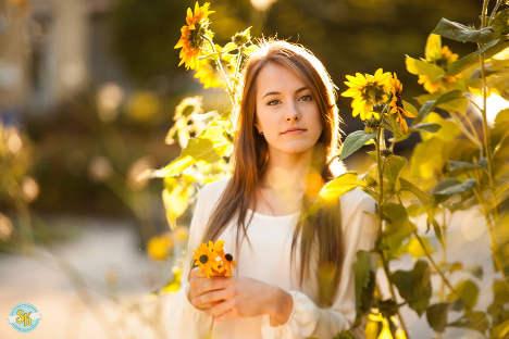 woman standing in sunflower field holding two sunflowers looking at camera