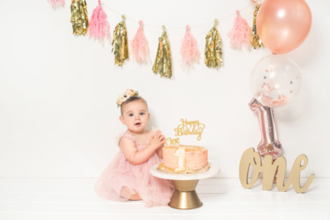 young girl sitting behind a birthday cake with pieces of decor around