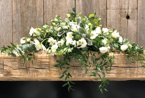 white flower bouquet sitting on a wooden mantle with greenery hanging over the side