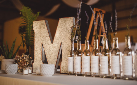 wedding table set up with large m and many wine bottles to the right
