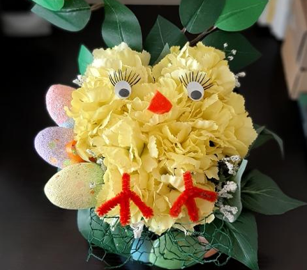 yellow flower with easter egg decor to the left and crafted to look like a chicken with pipe cleaner and googly eyes