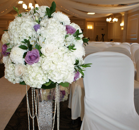 large flower bouquet in tall vase at a wedding venue with white and purple flowers and greenery popping through in some areas