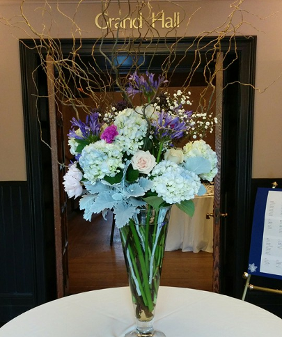 large flower bouquet in tall vase with white purple and pink flowers with thin twigs coming out of the top