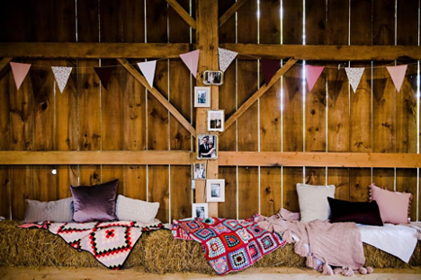 event setup in a barn with bails of hay with blankets and pillows and triangle banner on top beam