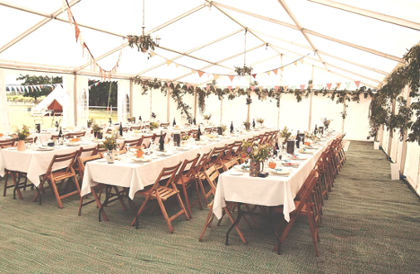 event setup with three long tables set for dinner with greenery and banners hanging from ceiling in a tent