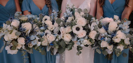 Bridal party holding wedding bouquets with white and blue flowers with greenery coming through