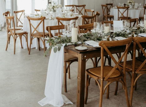 wedding round table set up with wooden chairs, tables, and greenery in the middle of the table set for dinner