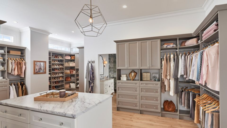 interior of a large walk in closet with island, shelving, cabinets, and clothes sorted and put away