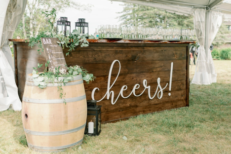wedding bar station with wooden barrel to the left with menu and many wine glasses on the bar top