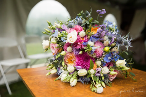 large wedding event bouquet with pink, purple, white and orange flowers with greenery throughout on a table