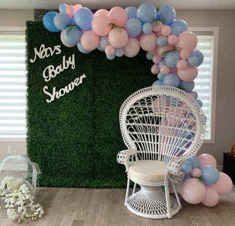 faux grass backdrop with large wicker white chair and pink and blue balloon garland on the right