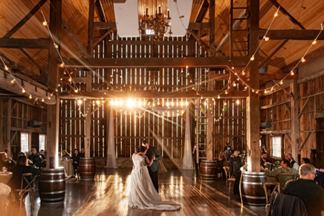 large barn wedding with bride and groom dancing with many string lights and brown wooden accents