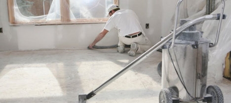 Man wearing all white in a renovated home laying something on the floor in front of a vacuum
