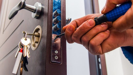 Man working with screwdriver to fix a lock with keys hanging from the door
