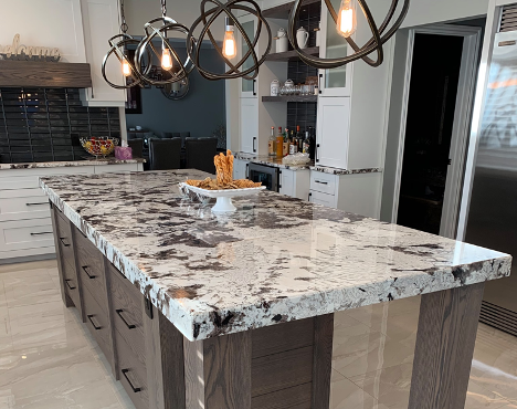 long kitchen island with patterned granite countertop with overhead lights on