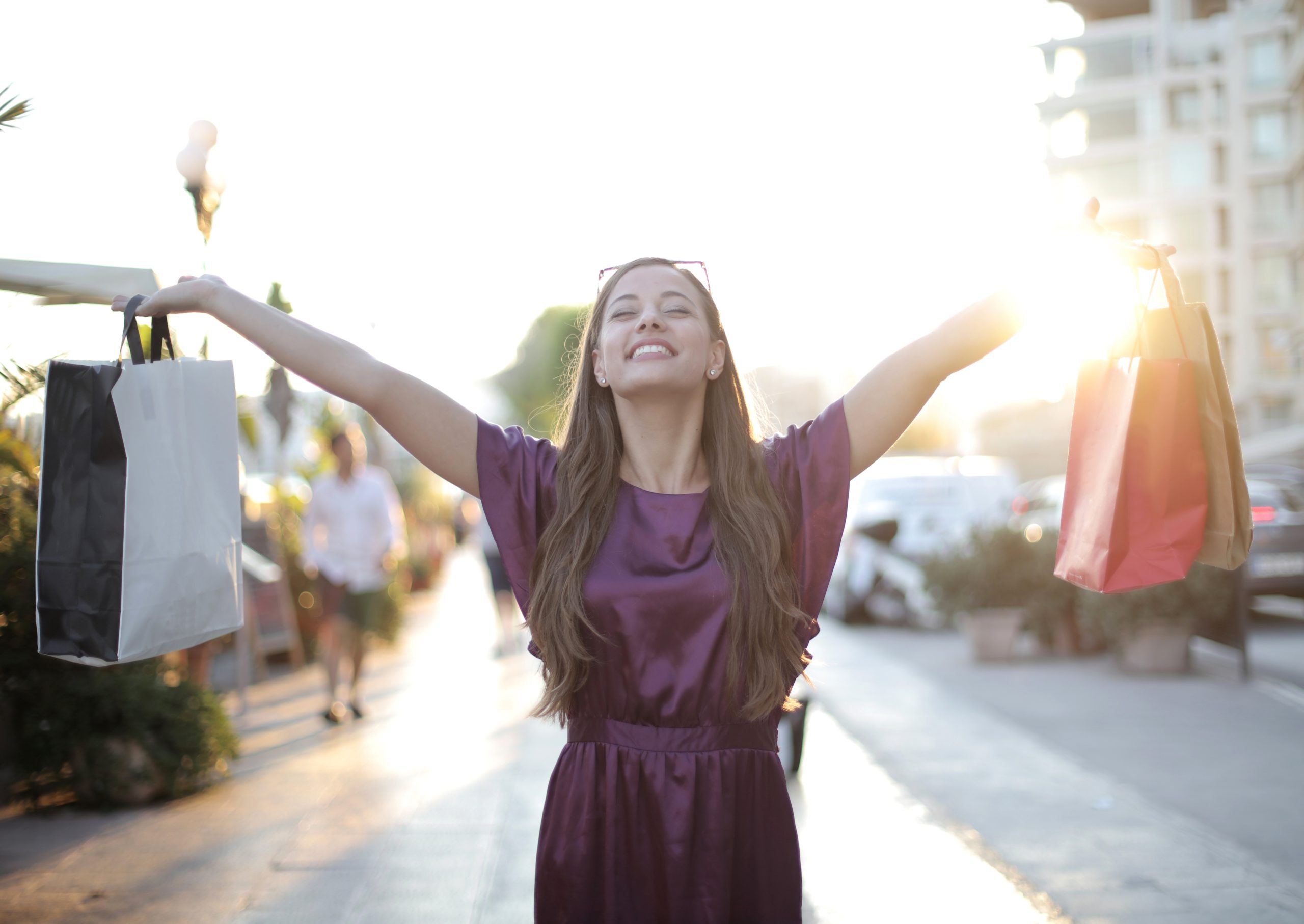 Woman smiling with shopping bags in each hand with arms raised up on a sunny day